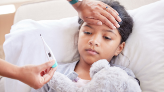 Mãe com um termómetro a medir febre a uma criança eitada na cama.